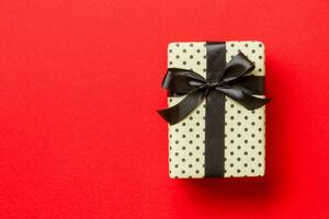 Top view Christmas present box with black bow on red background with copy space photo