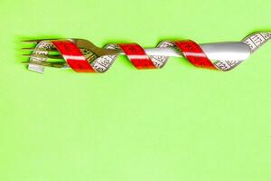 Close up of fork wrapped with tape measure on green background. Top view of obesity concept photo