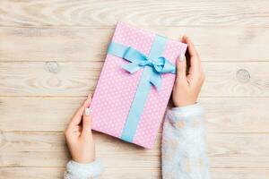 Woman arms holding gift box with colored ribbon on yellow rustic wooden table background, top view and copy space for you design photo