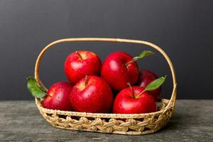 Ripe garden apple fruits with leaves in basket on wooden table. Top view flat lay with copy space photo