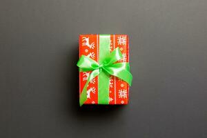 wrapped Christmas or other holiday handmade present in paper with green ribbon on black background. Present box, decoration of gift on colored table, top view with copy space photo