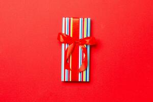 Gift box with red bow for Christmas or New Year day on red background, top view with copy space photo