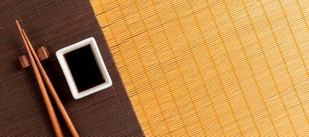 Chopsticks and bowl with soy sauce on two bamboo mat blak and yellow top view with copy space photo