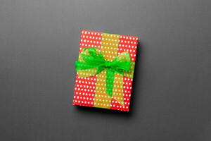 wrapped Christmas or other holiday handmade present in paper with green ribbon on black background. Present box, decoration of gift on colored table, top view with copy space photo