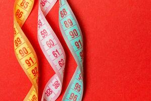 Top view of spiral colorful measure tapes on red background. Concept of perfect female figure with empty space for your idea photo