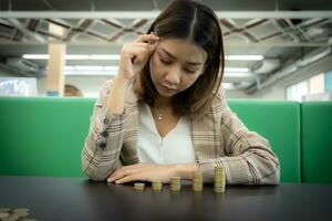 Beautiful asian girl is think about how to get more profit  by symbolizing coins on her desk, Saving money concept. photo