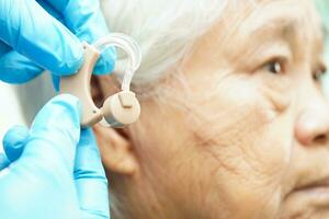 Doctor install hearing aid on senior patient ear to reduce hearing loss problem. photo