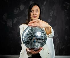 Portrait of a woman holding a silver disco ball. Taken in a photo studio.