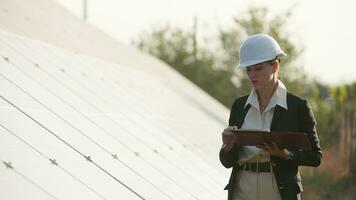 mujer de negocios trabajando en comprobación equipo a solar poder planta con tableta Lista de Verificación, teléfono inteligente hembra trabajando en un innovador más eficiente solar panel batería concepto. video