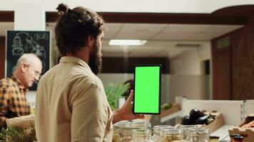 Mann mit isoliert Bildschirm Smartphone im Null Abfall Supermarkt zu prüfen Zutaten zum gesund Rezept. Klient im lokal Lebensmittelgeschäft Geschäft Verwendet Attrappe, Lehrmodell, Simulation Handy, Mobiltelefon Telefon während Einkaufen zum organisch Gemüse video