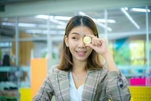 hermosa asiático negocio mujer sostener un moneda en su uno mano y cubierto en su ojos con un sonrisa en su rostro. foto