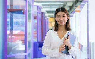 hermosa asiático negocio mujer es en pie frente a el cámara mientras participación un tableta con un contento expresión y un sonrisa, digital marketing. foto