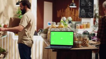 Chroma key laptop with copy space used as commercial sign in local shop using renewable energy. Promotional ad on green screen device in food store with products in repurposable metal containers video