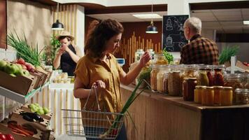 Zero waste supermarket customer roaming around aisles adding healthy natural pantry staples to shopping basket, dolly in shot. Local grocery shop client shopping for chemicals free bulk food items video