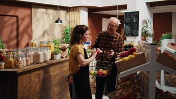 Sustainable zero waste supermarket seller assisting aged client, adding needed food items to shopping basket. Storekeeper helping old man in local shop, teaching him how to prepare bought ingredients video