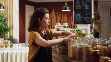 ritratto di sorridente zero rifiuto supermercato proprietario utilizzando biodegradabile bicchiere contenitori per suo massa cibo per inferiore clima impatto. allegro donna nel Locale drogheria negozio organizzazione merce video