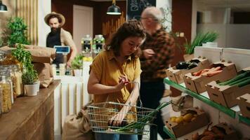 Null Abfall Supermarkt Kunde wandernd um Gänge Hinzufügen organisch Gemüse zu Einkaufen Korb. lokal Gegend Geschäft Klient Einkaufen zum Pestizide kostenlos Essen Artikel video