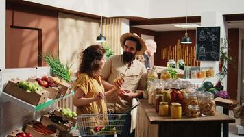 Portrait of happy vegan couple buying pantry staples from zero waste supermarket. Smiling clients shopping for bulk food products in reusable jars from local neighborhood store, zoom in shot video