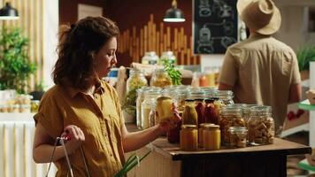 Portrait of smiling woman in eco friendly zero waste supermarket using shopping basket to purchase bulk items in ecological glass containers. Client in local grocery shop buying chemicals free food video