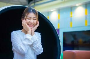 Beautiful asian business woman is sitting in a modern round chair with both hands resting on her cheeks and a smile on her face, Digital marketing, Copy space. photo