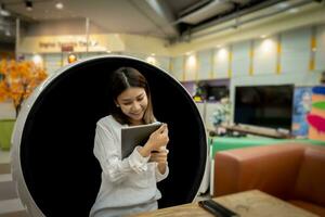 Beautiful businesswoman is happy to receive a vacation message from her boss via tablet while sitting in a modern round chair in the living room with a smile. photo