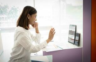 hermosa asiático en línea vendedor es saludo el audiencia en un En Vivo transmitir mientras sentado en su oficina. foto