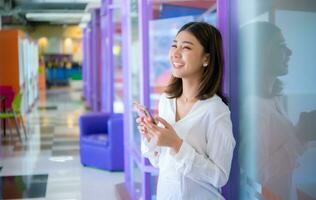 Beautiful asian business woman stands confidently holding her mobile phone in her hand and looking to the copy space, Digital marketing. photo