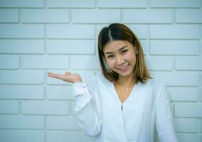 Beautiful asian business woman standing with a smile while looking to the camera against a white brick background, Digital marketing. photo