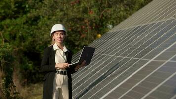 Portrait of electrician woman engineer in safety helmet using laptop checking solar panels. Female technician at solar station. Photovoltaic power station concept video