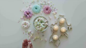 oben Aussicht Tasse von heiß Schokolade. Marshmallows im Becher mit Kakao. bunt Donuts auf ein Weiß Tabelle umgeben mit Kerzen video