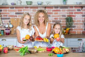 Mother and daughters cooking together in the kitchen. Healthy food concept. Portrait of happy family with fresh smoothies. Happy sisters. photo