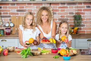 Mother and daughters cooking together in the kitchen. Healthy food concept. Portrait of happy family with fresh smoothies. Happy sisters. photo