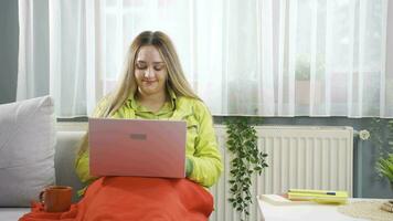frio jovem mulher às casa bebendo café e usando computador portátil. video