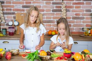 Two little girls in the kitchen with fresh vegetables. Healthy food concept. Happy sisters. photo