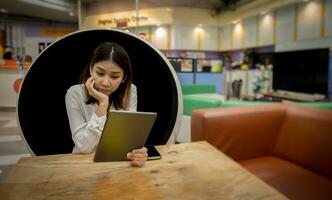 Beautiful asian businesswoman she is stressed about this month's performance that did not turn out well while sitting in a modern round chair and holding tablet in the living room. photo