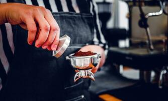 Barista holding portafilter and coffee tamper making an espresso coffee in cafe photo