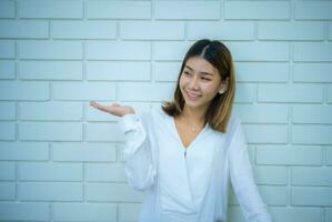 Beautiful asian business woman standing and looking to the copy space with a smile gainst a white brick background, Digital marketing. photo