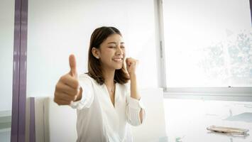 Cheerful beautiful asian businesswoman thumbs up to the camera with smile on her face. photo