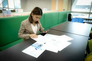 Beautiful asian businesswoman is sitting and holding tablet with serious face in her office. photo