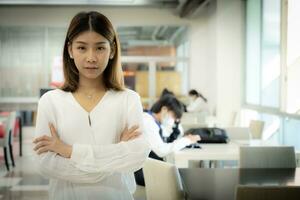 The beautiful asian female teacher is standing with arms crossed and looking at the camera with a serious face in the library room. photo