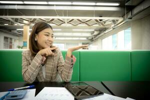 Beautiful asian businesswoman points her finger and looks at the open hand with copy space with a surprised expression in her office. photo