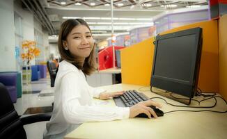 hermosa asiático oficina mujer contento a trabajo con sonrisa en corporativo oficina. foto