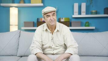 Old man sitting on sofa thinking about happy moments and smiling. video