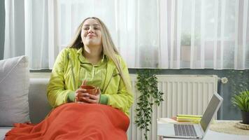 The young woman drinking coffee leaning against the heater is cold. video