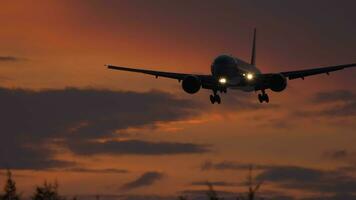 silhouette de air avion atterrissage à nuageux le coucher du soleil avec magnifique rouge ciel et Soleil dans Contexte video