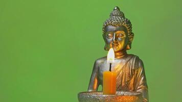 a buddha statue with a lit candle on a green background video