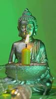 vertical video of a silver buddha statue with a candle and a green background