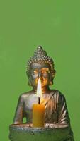 vertical video of a silver buddha statue with a candle and a green background