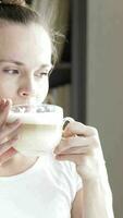 a woman is drinking from a cup of coffee while standing beside the window video