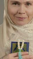 un mujer en un hijab participación un libro y un oración rosario video